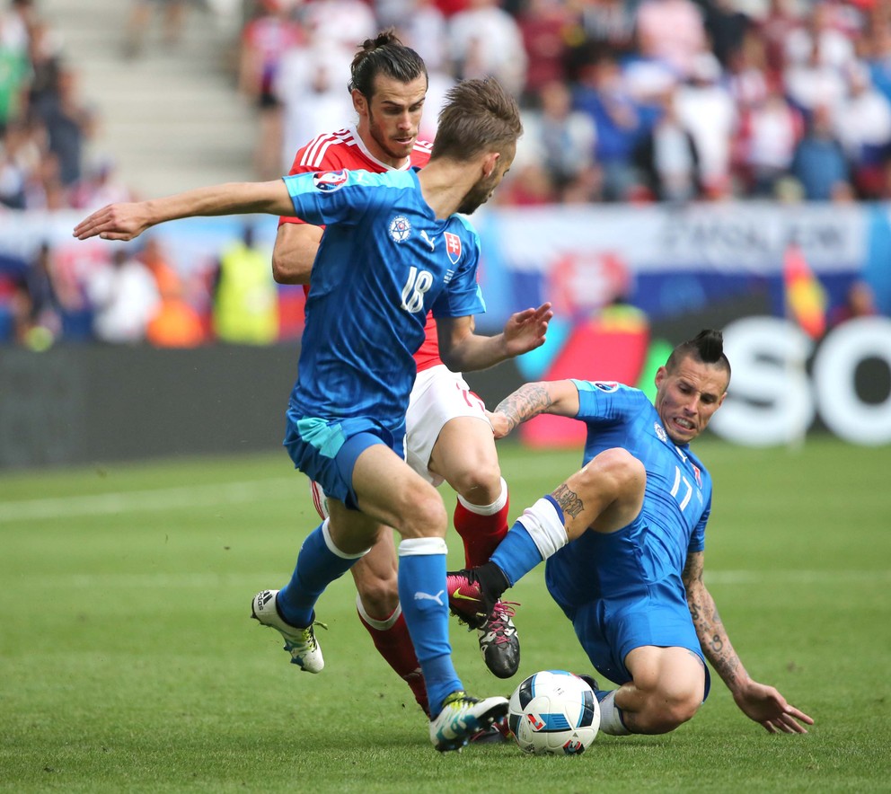Marek Hamšík (vpravo) prestrkáva loptu na Dušana Šventa (s číslom 18). Zastaviť akciu Slovenska sa snaží Gareth Bale.