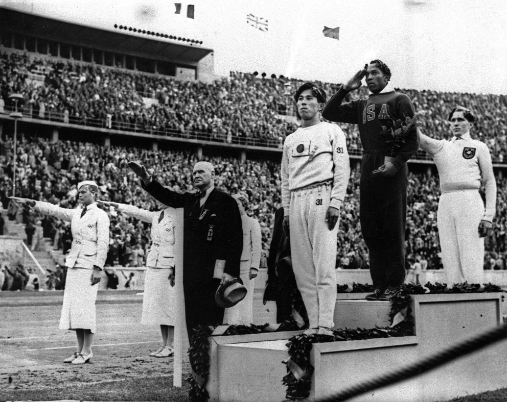 Jesse Owens (na stupni víťazov v strede).