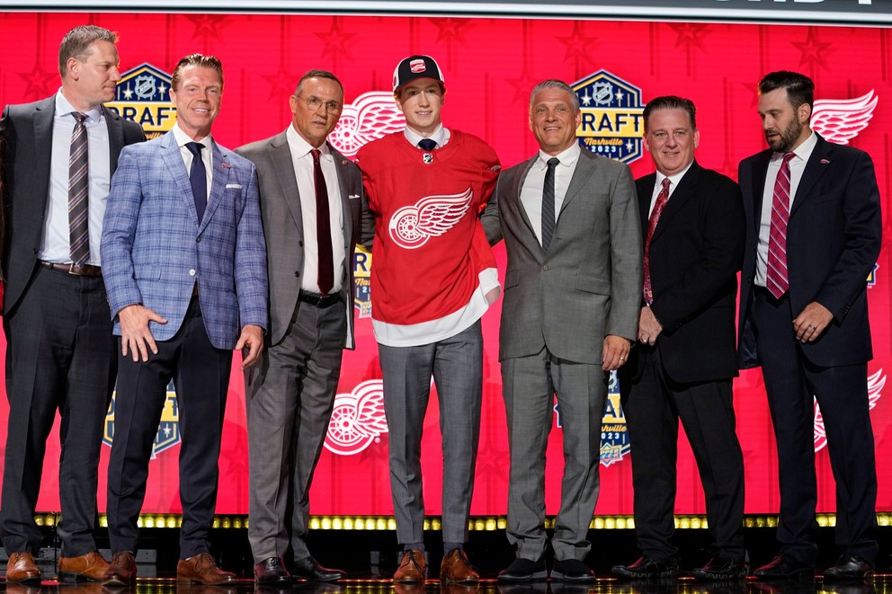 Deviatka draftu NHL 2023 Nate Danielson pózuje s predstaviteľmi Detroitu Red Wings.