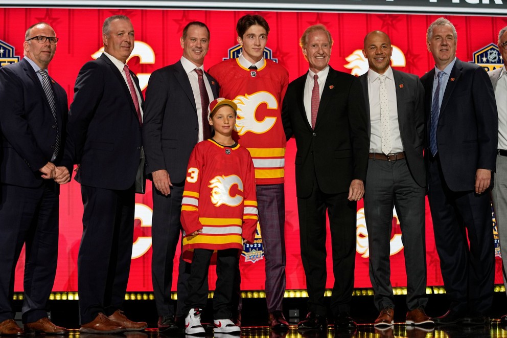 Samuel Honzek pózuje v drese Calgary Flames spolu predstaviteľmi klubu po tom, ako si ho vybrali zo 16. miesta počas vstupného draftu NHL 2023.