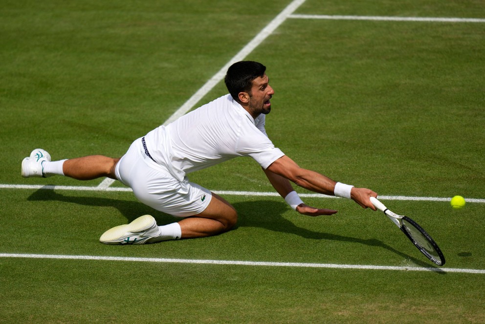 Novak Djokovič padá pri odvrátení loptičky na londýnsku trávu.