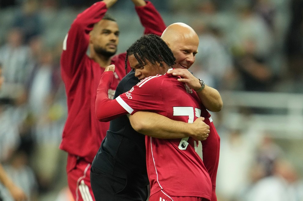 Tréner Liverpoolu Arne Slot (uprostred) a hráč z Liverpoolu Rio Ngumohasa sa objímajú po góle