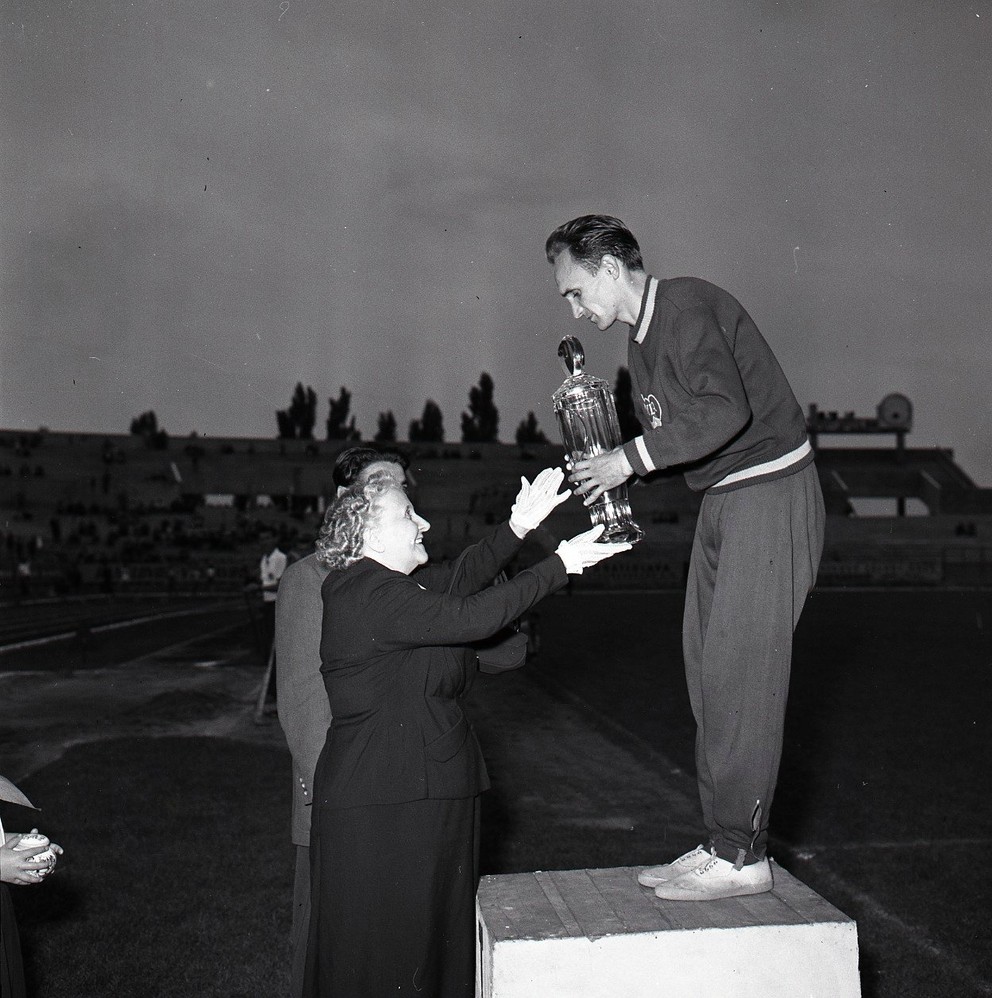 Dušan Čikel preberá z rúk vdovy po Jánovi Hajdócym veľký brúsený pohár za víťazstvom v pretekoch na 1500 m na prvom ročníku atletického mítingu Cena Pravdy v roku 1957. Hlavná disciplína mítingu niesla názov Memoriál Jána Hajdócyho po známom trénerovi, pedagógovi a veľkom propagátorovi atletiky. 
