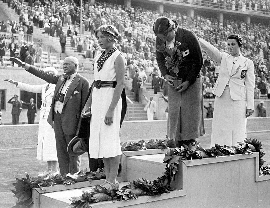 August 1936. Medailový ceremoniál na olympijskom štadióne v Berlíne. Inge Sørensenová v popredí v bielych šatách, v tom čase mala 12 rokov a jeden mesiac.