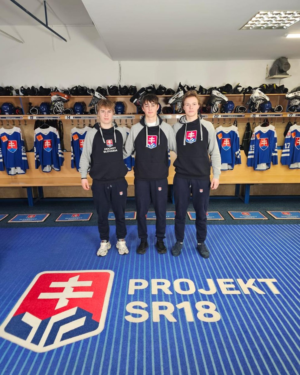 Zľava Kristian Rezničák, Matúš Válek a Max Melicherík v šatni slovenskej hokejovej reprezentácie do 18 rokov. 